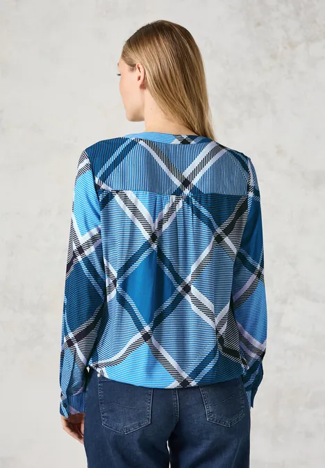 Frau mit langem Haar trägt ein blau kariertes Hemd und Jeans, Rückenansicht.
